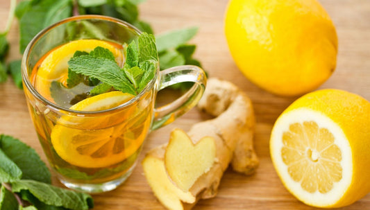 Green tea, mint, ginger, and lemon laid out on a wooden surface.