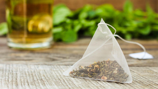An organic peppermint tea bag sitting in the foreground, a bed of peppermint in the background.